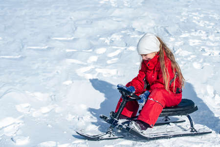 Child enjoying the ski slopes. Little girl enjoy a sleigh ride. Toddler kid girl riding a sledge. Children play outdoors in snow. Kids sled in mountains in winter. Outdoor fun Christmas vacation.の写真素材