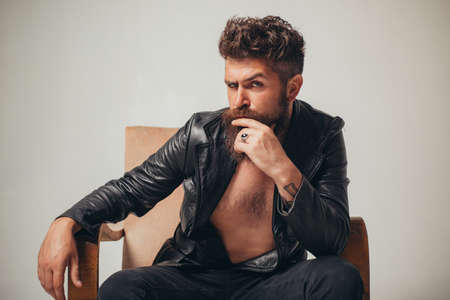 Sexy man. Dandy fashionista in night club. Serious confident ambition concentrated focused handsome stubble man in modern jacket sit on couch. Respectable mens beauty, fashion. Young hipster.の写真素材