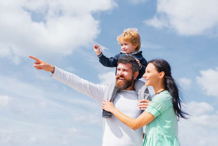 Daddy, mommy and child son. Happy family - child son playing with paper airplane. Portrait of happy father giving son piggyback ride on his shoulders, hug wife and looking up.の写真素材