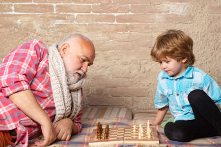 Little boy playing chess with his Grandfather. Chess piece. Senior man thinking about his next move in a game of chess.の写真素材