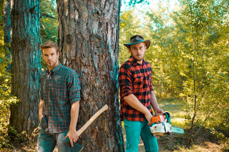 Foresters in the forest. Hipsters on serious face carries axe. Lumberjack brutal holds axe. Brutal...