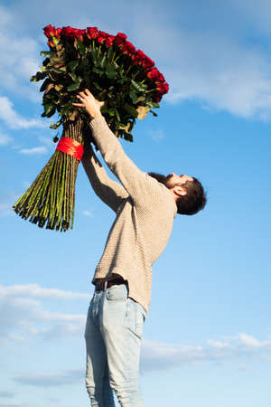 Man with Big bouquet of roses. Celebrate Valentines Day and Romantic Gifts. Handsome guy is holding bouquet of big red roses. Handsome man giving flowers to his lover on Valentines Day.の写真素材