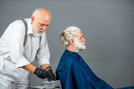 Senior hairdresser applying dye to man hair. Process of a guy having his hair dyed at hairdresser....