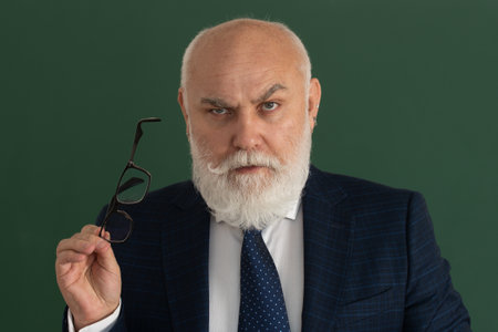 Professor or serious teacher. Elderly man teacher on a blank chalkboard during lesson, teaching class at college. Think senior.の写真素材