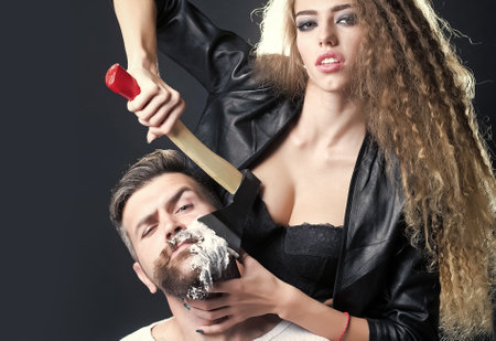 Sensual woman shaving bearded haired man with beard and foam with axe.の写真素材
