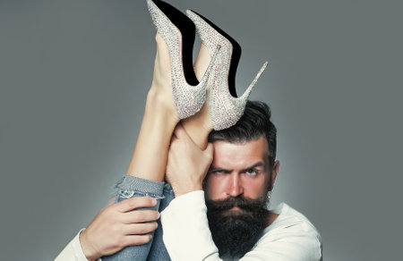 Man holding legs of woman. Portrait of handsome man with beard moustache eyebrow. Diamante high heels.の写真素材
