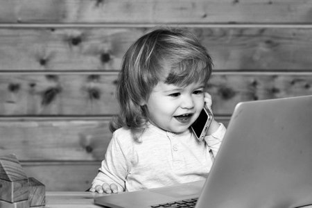 Happy baby boy child playing on notebook and mobile phone near toy building blocks indoors.の写真素材