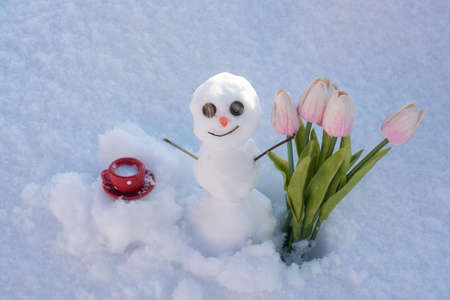 Winter weather. Spring snowman with coffee cup and flowers.の写真素材
