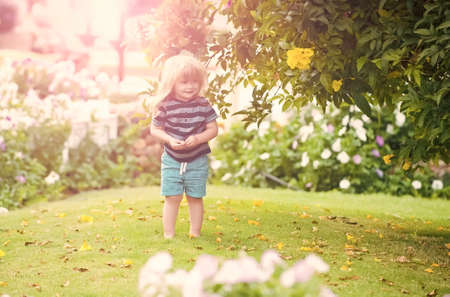 Kid baby outdoor in garden with flowers and green grass on natural background, summer kids vacation, childhood and happiness.の写真素材
