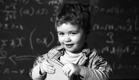 Smart child on smiling face, holds book in hands. Pupil, preschooler on chalkboard, kid likes to study.の写真素材