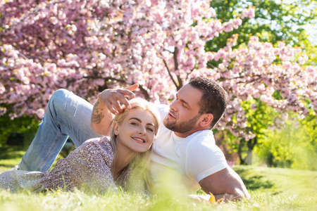 Happy spring couple in love having fun. Two young people relaxing in sakura flowers. Smiling lovers relaxing in park. Family over nature blossom background. Relationships and dating.の写真素材