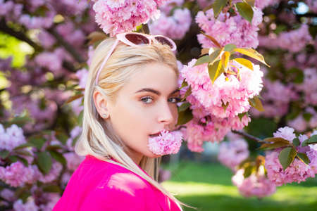 Beautiful girl in pink flowers in summer blossom park. Portrait of young woman in the flowered garden in the spring. Tongue sensual.の写真素材