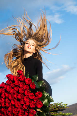 Beautiful girl on sky background. Girl and roses. Favorite flowers. Gift with love. Happy girl hugs a bouquet. Valentine day present.の写真素材