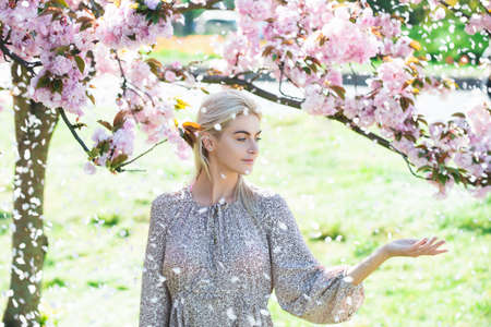 Beautiful girl in pink flowers in summer blossom park. Beauty woman in pink cherry garden on a...