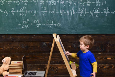 Little child writing on chalkboard. Kid in front of board with math equation. Smart pupil studying...