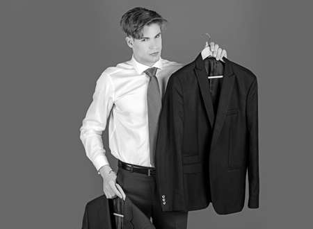 Young businessman in white shirt and tie, shop assistant present formal jacket outfit on hanger, choice and success, business fashionの写真素材
