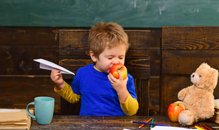 Kid eating apple with pleasure in class. Cute boy biting fruit with his eyes closed. Infant playing...