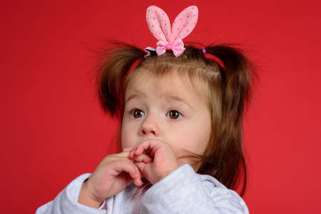 Cute easter bunny baby with rabbit ears and pigtails isolated on red background.