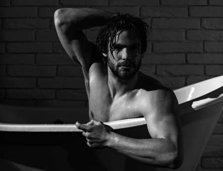 Guy with wet hair sitting in bath tub. Hygiene and healthcare. Sexy man with muscular body in bathtub.の写真素材