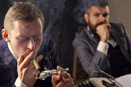 Man lighting cigar from burning dollar banknote. Business meeting. Gangster and money. Concept of crime. Smoky background. Retro and vintage style.の写真素材