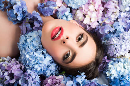 Woman beauty. Girl lying on flowers. Unity with nature. Blossom. Makeup cosmetics and skincare.