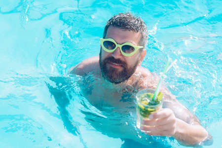 Man with mojito. Cocktail party with bearded man in pool. Pool party with hipster in blue water. Relax at sea and spa resort.の写真素材