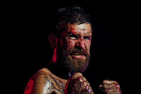 Angry man with blood paint on angry face. Hipster in fight position with fists on black background. Sport, boxing, fighting. Power man.の写真素材
