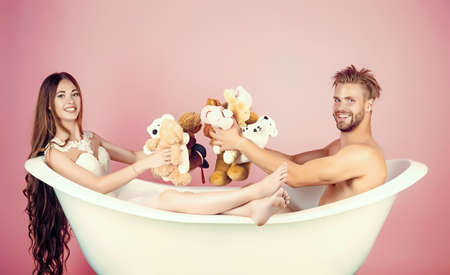 Couple in bath. Boyfriend and girlfriend relax in bathtub on pink background. Man in bath tub near girl with long hair. Love and romance.の写真素材