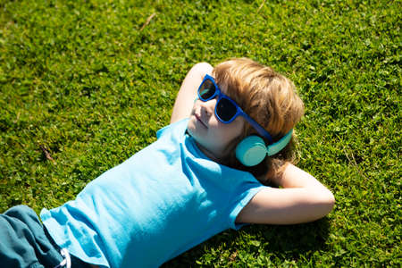 Summer chill boy in headphones. Listening to music. Kid in park lying on grass.