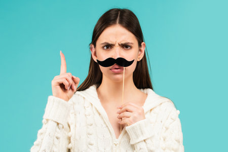 Woman with fake mustache having fun. Funny female actress with finger up isolated on blue background.の写真素材
