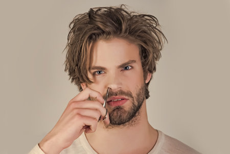 Man trimming nose hair with scissors and tweezers. Guy trimming his nose hair with scissors.