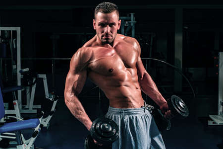 Gym. Bodybuilding. Training and workouts. Dumbbells exercises. Male torso with six packs. Sportsman with naked body.の写真素材