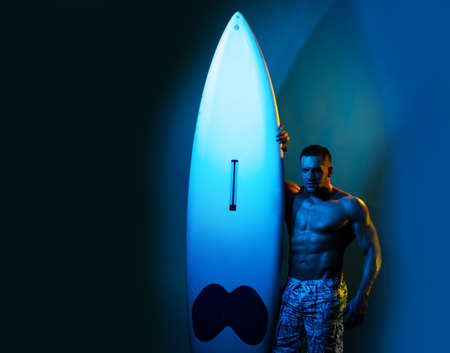 Sexy man with serf board. Male serfer with fit and firm body. Neon surfboard light background.の写真素材
