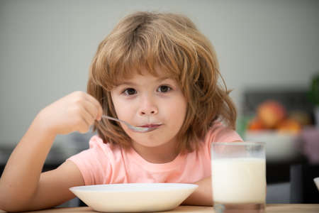 Closeup face of kid eating organic food, yogurt, milk. Child healthy eat. Smiling little boy eating food on kitchen.の写真素材