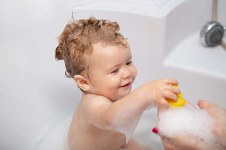 Bathing baby. Happy kid with soap foam on head. Child bubble bath.
