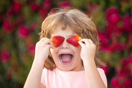 Child fun with strawberries. Happy funny child holding strawberries in the summer outdoor.の写真素材