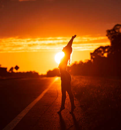 Black silhouette of pretty girl or beautiful woman, sexy slim model, with long hair poses on sea beach at sunset outdoors on violet sky backgroundの写真素材