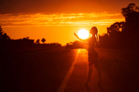 Black silhouette of pretty girl or beautiful woman, sexy slim model, with long hair poses on sea beach at sunset outdoors on violet sky backgroundの写真素材