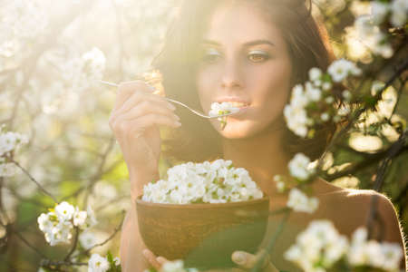 Pretty vegan woman with dish of cherry bloom blossom leaves. Healthy eating concept. Dieting, vegeterian.の写真素材