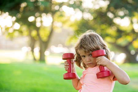 Children sporty lifestyle activity. Boy workout with dumbbell in park. Kid sport. Child exercising outdoor.の写真素材