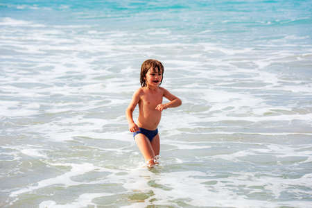 Kid boy playing on the beach on summer holidays. Children in nature with beautiful sea. Happy kids on vacations at seaside running in the water.の写真素材