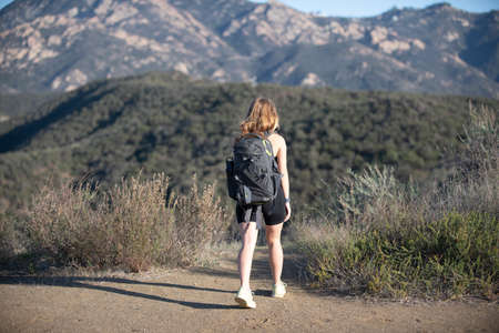 Pretty girl hiker hiking in summer dress travel with backpack on mountain or cliff hill peak.の写真素材