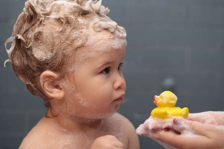 Hygiene and body care for children. Washing adorable baby in bathroom. Kid with soap suds on hair taking bath. Closeup portrait of smiling kid, health care and kids hygiene.の写真素材