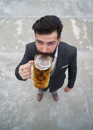 Full length, wide angle. Funny man drinking beer from a glass mug.の写真素材
