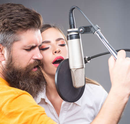 Singer couple is performing a song with a microphone while recording in a music studio.の写真素材