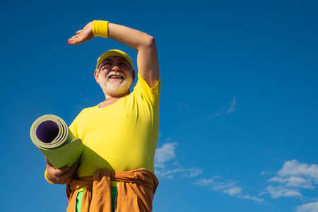 Elderly man practicing sports on blue sky background. Sporting. Healthy and sport. Grandfather pensioner. Like sports.の写真素材