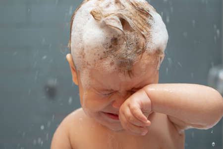 Washing adorable baby in bathroom. Kid with soap suds on hair taking bath. Closeup portrait of...