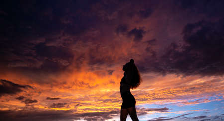 Black silhouette of pretty girl or beautiful woman, sexy slim model, with long hair poses on sea...