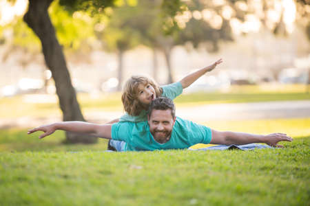 Concept of friendly family. Father lying on grass, with excited happy little child son on shoulder. Carefree two man generations family.の写真素材