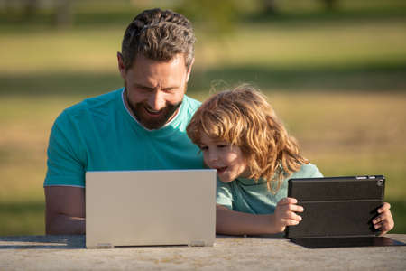Happy father using laptop relax with schooler son holding laptop have fun together, smiling dad and little boy child enjoy weekend with gadgets outside on nature.の写真素材